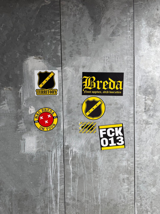 Diverse NAC Breda en Breda gerelateerde stickers op een metalen oppervlak bij het stadion, inclusief 'NAC TERRITORY', 'Breda Nooit opgeven, altijd doorzetten', 'NAC Breda on Tour' en 'FCK 013' stickers.