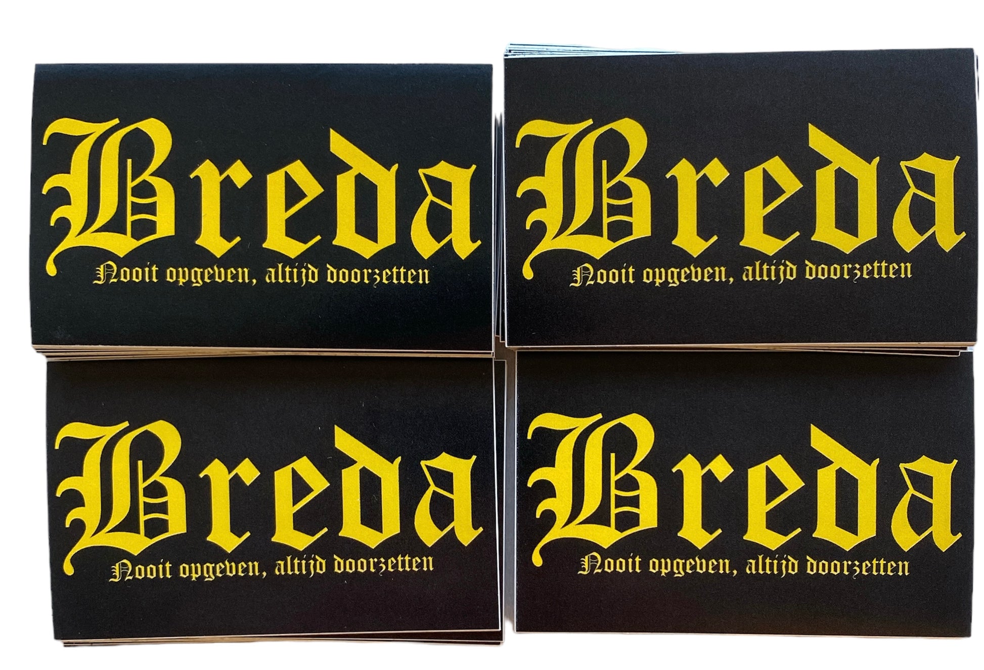 Deze foto toont vier stickers met het woord "Breda" in witte gotische letters en de tekst "Nooit opgeven, altijd doorzetten" eronder. Deze iconische spreuk is een motto van de club en symboliseert de vechtlust en vastberadenheid van NAC Breda. Deze stickers zijn perfect voor NAC Breda fans die hun clubliefde en verbondenheid met de stad Breda willen uiten. Ze zijn ideaal om te plakken op telefoons, laptops, auto's of andere persoonlijke spullen. Deze stickers zijn zwart met gele tekst