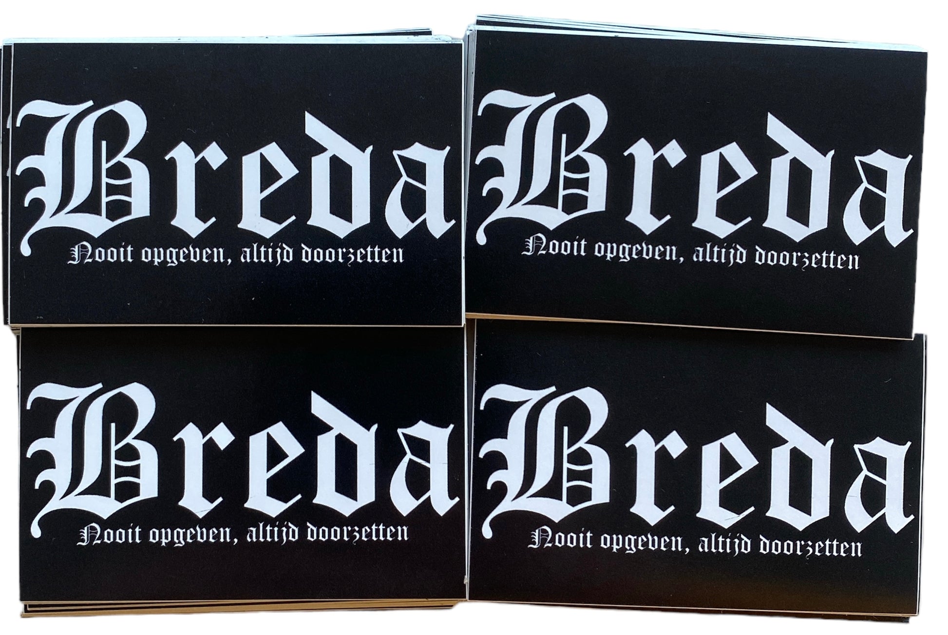 Deze foto toont vier stickers met het woord "Breda" in witte gotische letters en de tekst "Nooit opgeven, altijd doorzetten" eronder. Deze iconische spreuk is een motto van de club en symboliseert de vechtlust en vastberadenheid van NAC Breda. Deze stickers zijn perfect voor NAC Breda fans die hun clubliefde en verbondenheid met de stad Breda willen uiten. Ze zijn ideaal om te plakken op telefoons, laptops, auto's of andere persoonlijke spullen. Deze stickers zijn zwart met witte tekst
