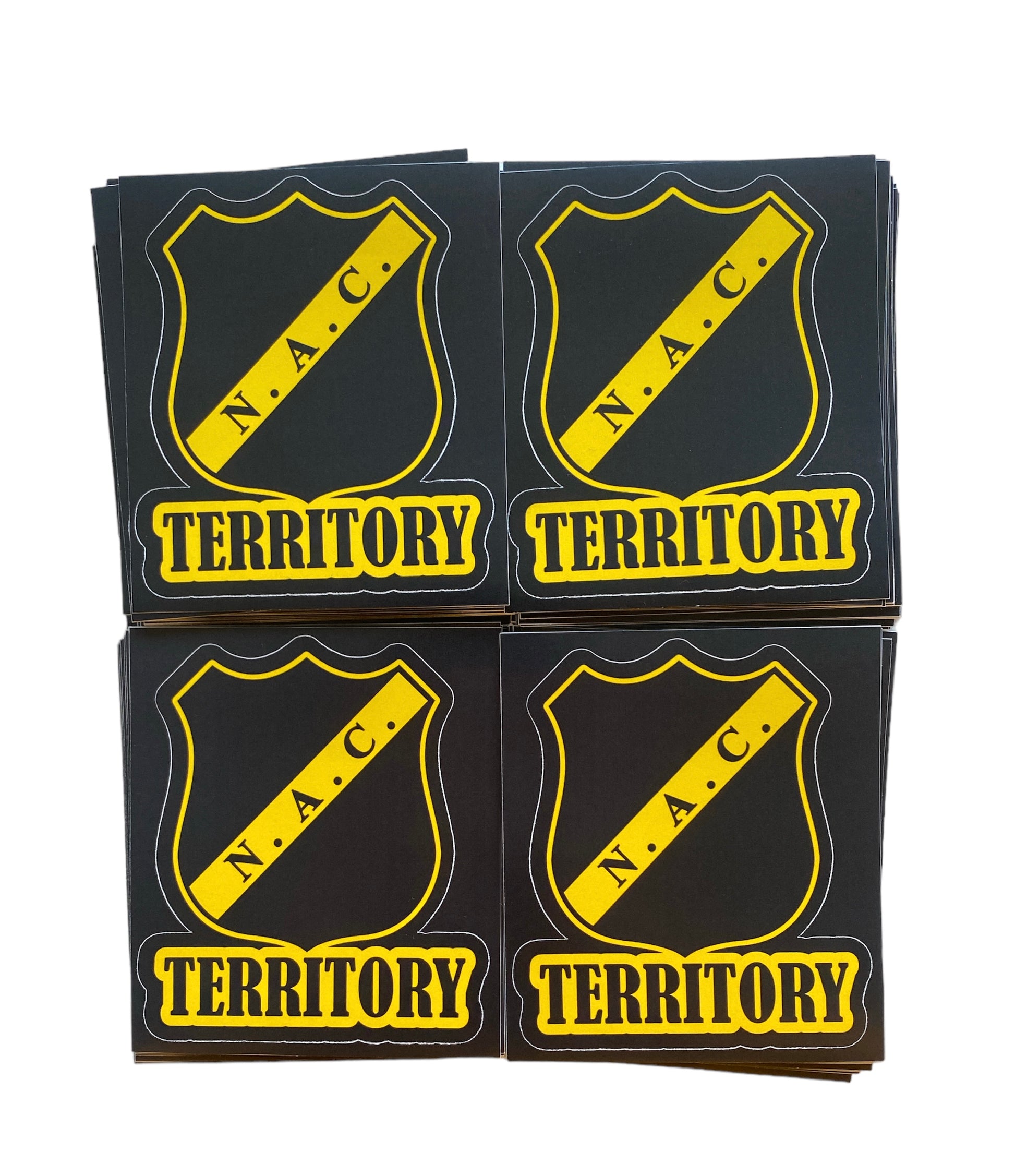 Deze foto toont vier stickers met het NAC Breda logo en de tekst "Territory". De stickers hebben een zwart-gele kleurenschema en een stoere uitstraling. Deze stickers zijn perfect voor NAC Breda fans die hun clubliefde en territorium willen claimen. Ze zijn ideaal om te plakken op telefoons, laptops, auto's of andere persoonlijke spullen.