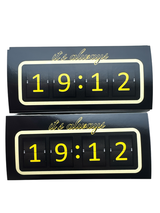 wee identieke rechthoekige stickers met een zwart design en een gele rand. De stickers tonen de tekst 'it's always' in script lettertype bovenaan, en daaronder de cijfers '19:12' in een digitaal klokstijl lettertype, gescheiden door stippen.
