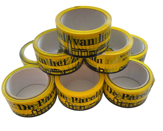 Deze foto toont een stapel rollen gele plakband met de tekst "De Parel van het Zuiden", de skyline en het wapen van Breda. Deze tape is perfect om dozen, pakketten en andere materialen mee dicht te plakken, en tegelijkertijd je clubliefde te tonen. De rollen zijn 6cm breed en 60 meter lang, waardoor ze ideaal zijn voor zowel kleine als grote verpakkingen.