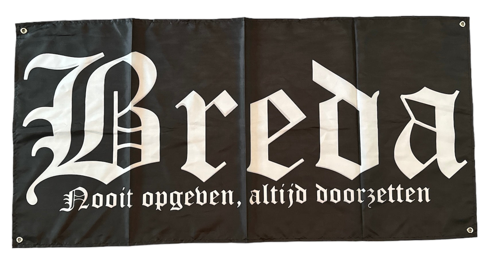 Deze foto toont een zwarte NAC Breda vlag met het woord "Breda" in witte gotische letters en de tekst "Nooit opgeven, altijd doorzetten" eronder. Deze iconische spreuk is een motto van de club en symboliseert de vechtlust en vastberadenheid van NAC Breda. Deze vlag is een perfecte manier om je steun te tonen aan NAC Breda en je verbondenheid met de stad Breda te uiten. Ideaal voor wedstrijden, sfeeracties en als decoratie. Deze vlag is zwart met witte tekst