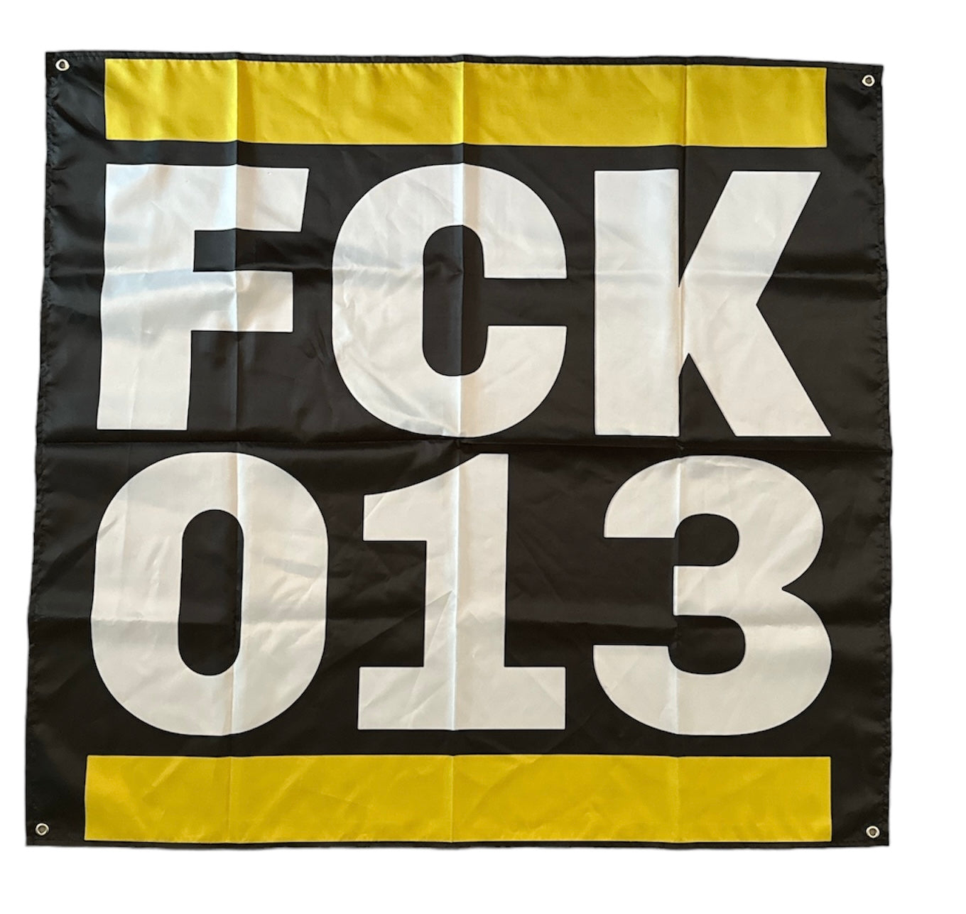 Deze foto toont een vierkante vlag met het opschrift "FCK 013" in witte, blokletterige letters tegen een zwarte achtergrond. De vlag heeft een gele rand aan de boven- en onderkant. "FCK" is een afkorting van een krachtterm, en "013" verwijst naar het netnummer van Tilburg, de stad van de aartsrivaal van NAC Breda, Willem II. Deze vlag is een provocerende uiting van clubliefde en rivaliteit, ideaal voor gebruik in het stadion of als decoratie