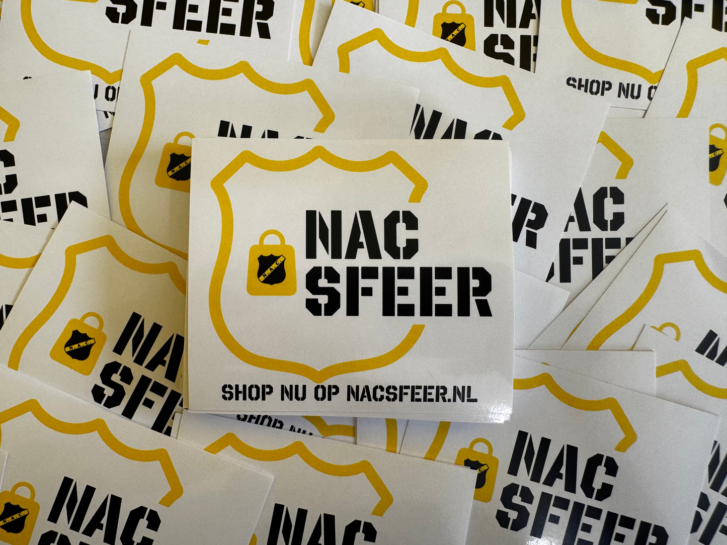 Stapel witte promotiestickers met het zwarte en gele NACsfeer logo, het slotje icoon en de webshoptekst 'Shop nu op NACsfeer.nl'.