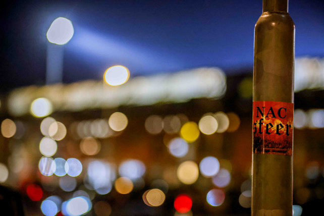 Een nacsfeer sticker geplakt op een lantaarnpaal met het nac stadion op de achtergrond