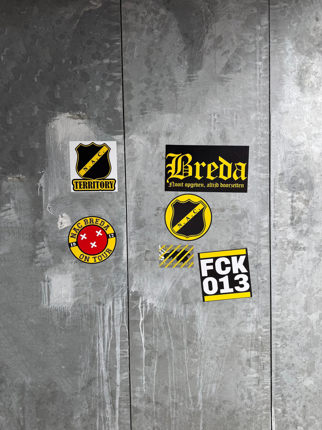 Diverse NAC Breda en Breda gerelateerde stickers op een metalen oppervlak bij het stadion, inclusief 'NAC TERRITORY', 'Breda Nooit opgeven, altijd doorzetten', 'NAC Breda on Tour' en 'FCK 013' stickers.