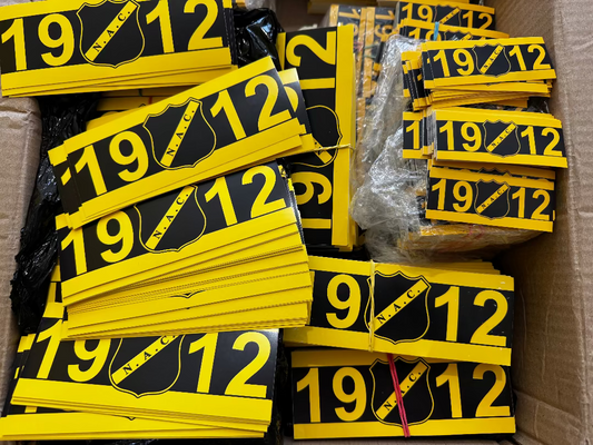 Geel-zwarte NAC Breda 1912 stickers opgestapeld in een doos, voorzien van het officiële NAC logo.