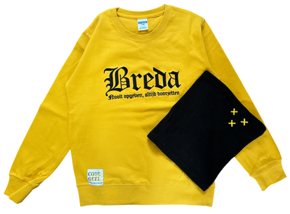 Een gele NAC Breda trui met de tekst 'Breda Nooit opgeven, altijd doorzetten' ligt naast een zwarte fleece nekwarmer met drie geborduurde gele Andreaskruisen op een donkere achtergrond