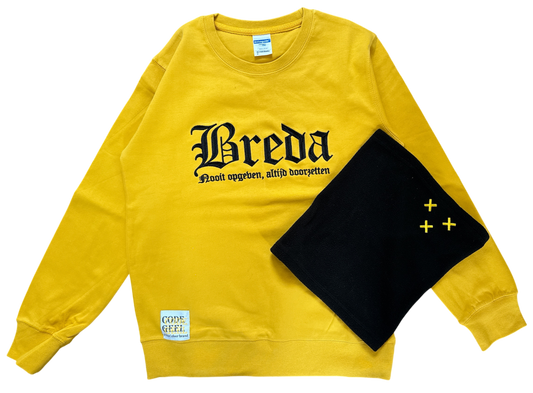 Een gele NAC Breda trui met de tekst 'Breda Nooit opgeven, altijd doorzetten' ligt naast een zwarte fleece nekwarmer met drie geborduurde gele Andreaskruisen op een donkere achtergrond