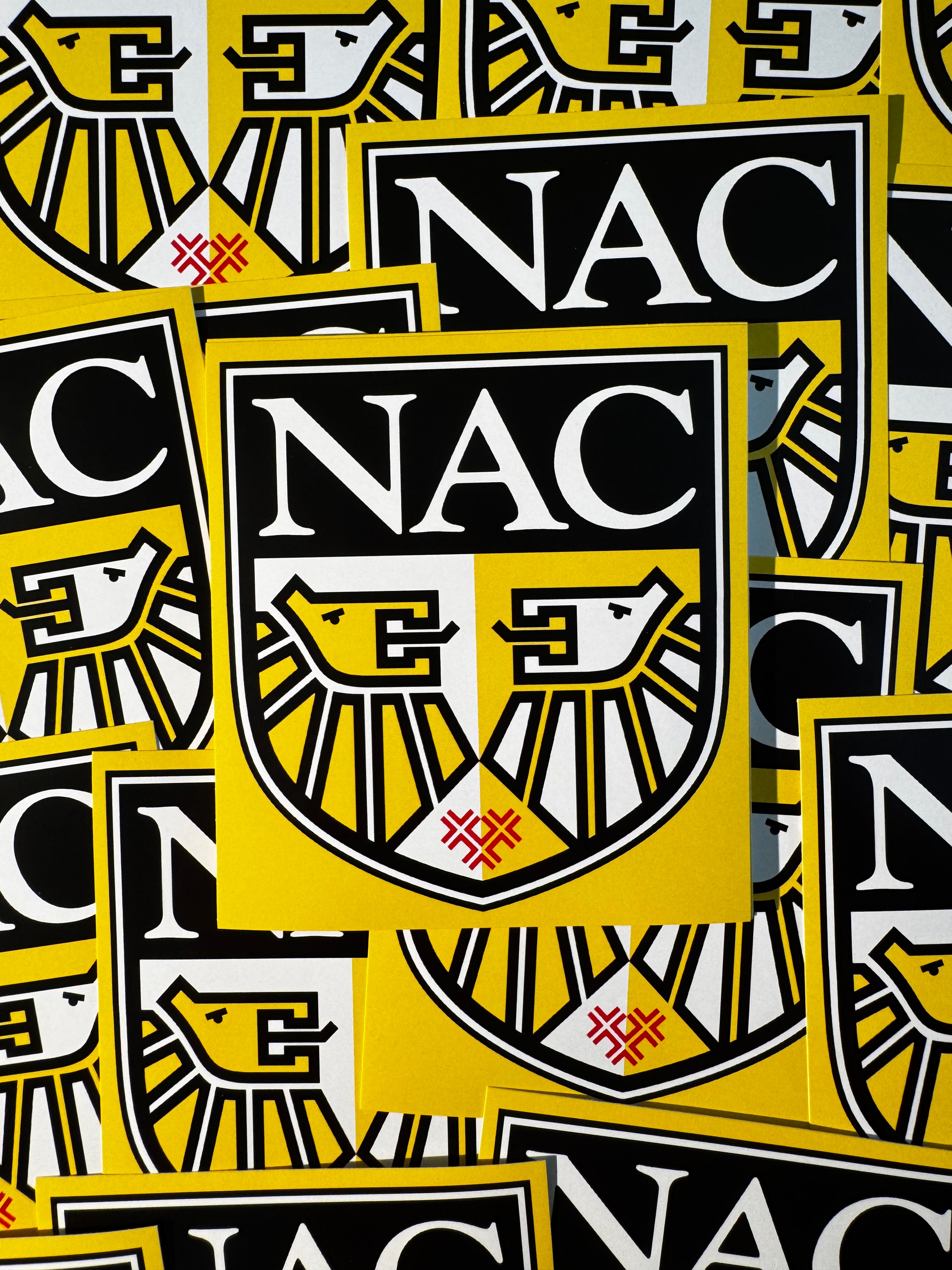 Stapel gele NAC stickers met het clublogo van 1996 tot 2012